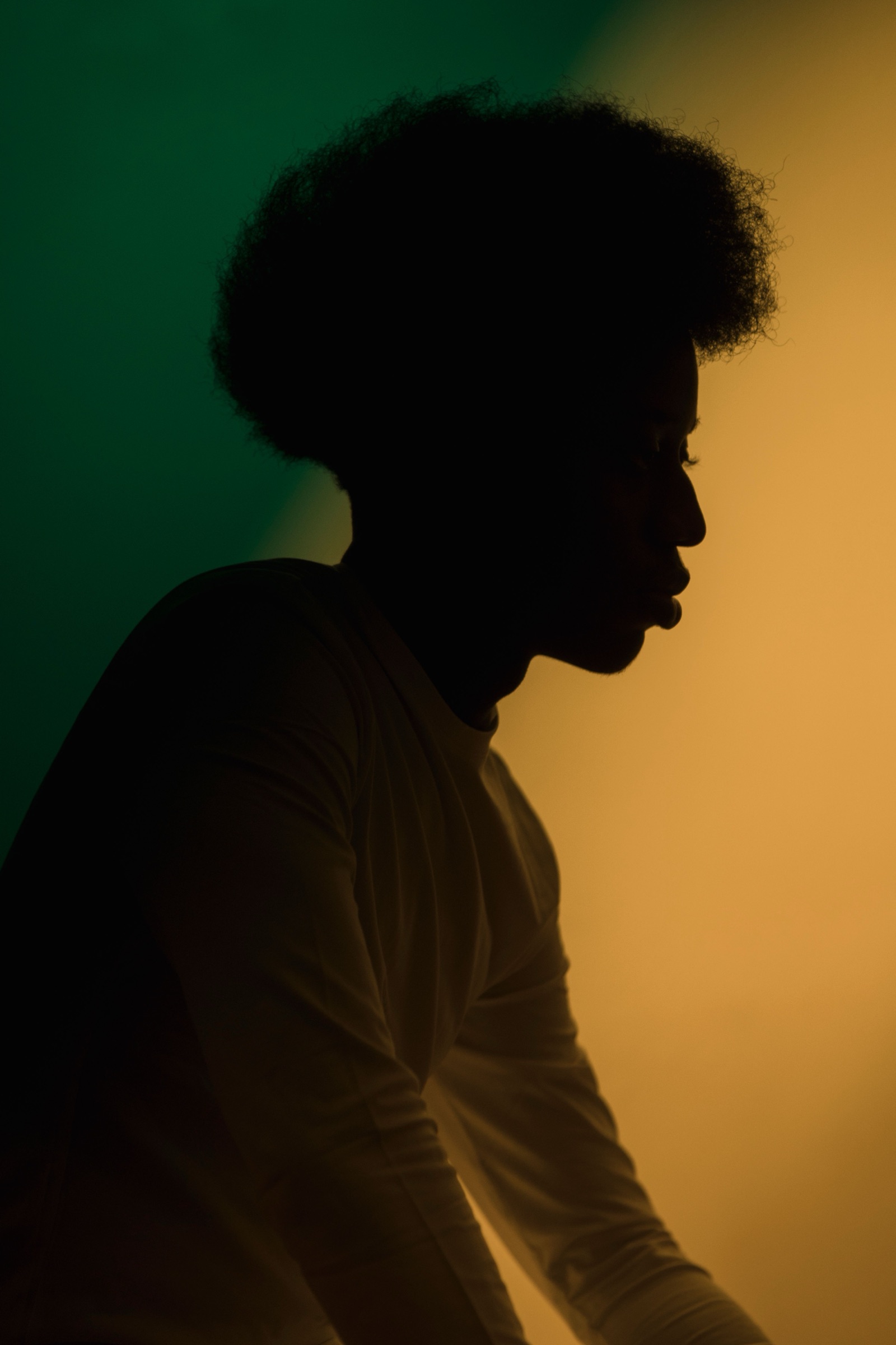 A young man in silhouette against a wash of green and gold