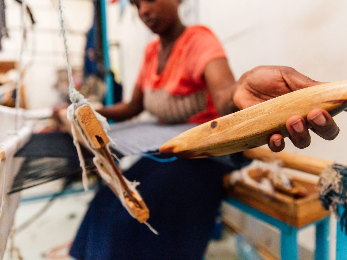 Hands passing a wooden shuttle across a loom